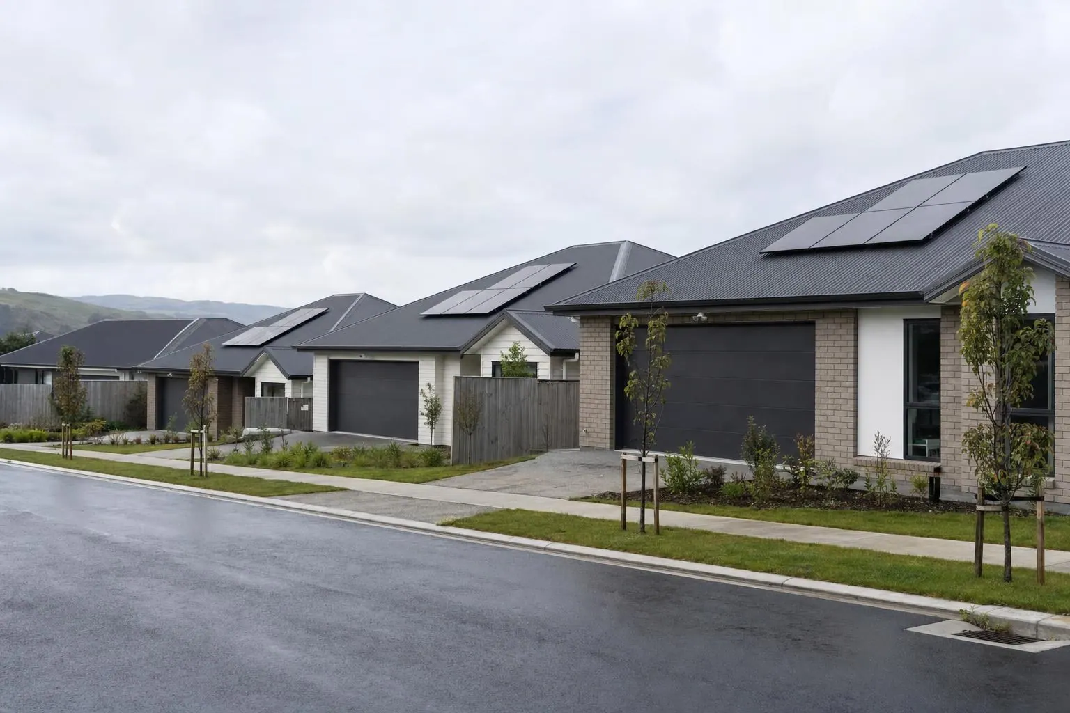 A row of new single-storey houses along a subdivision street, three of them with solar panels on their dark metal roofs